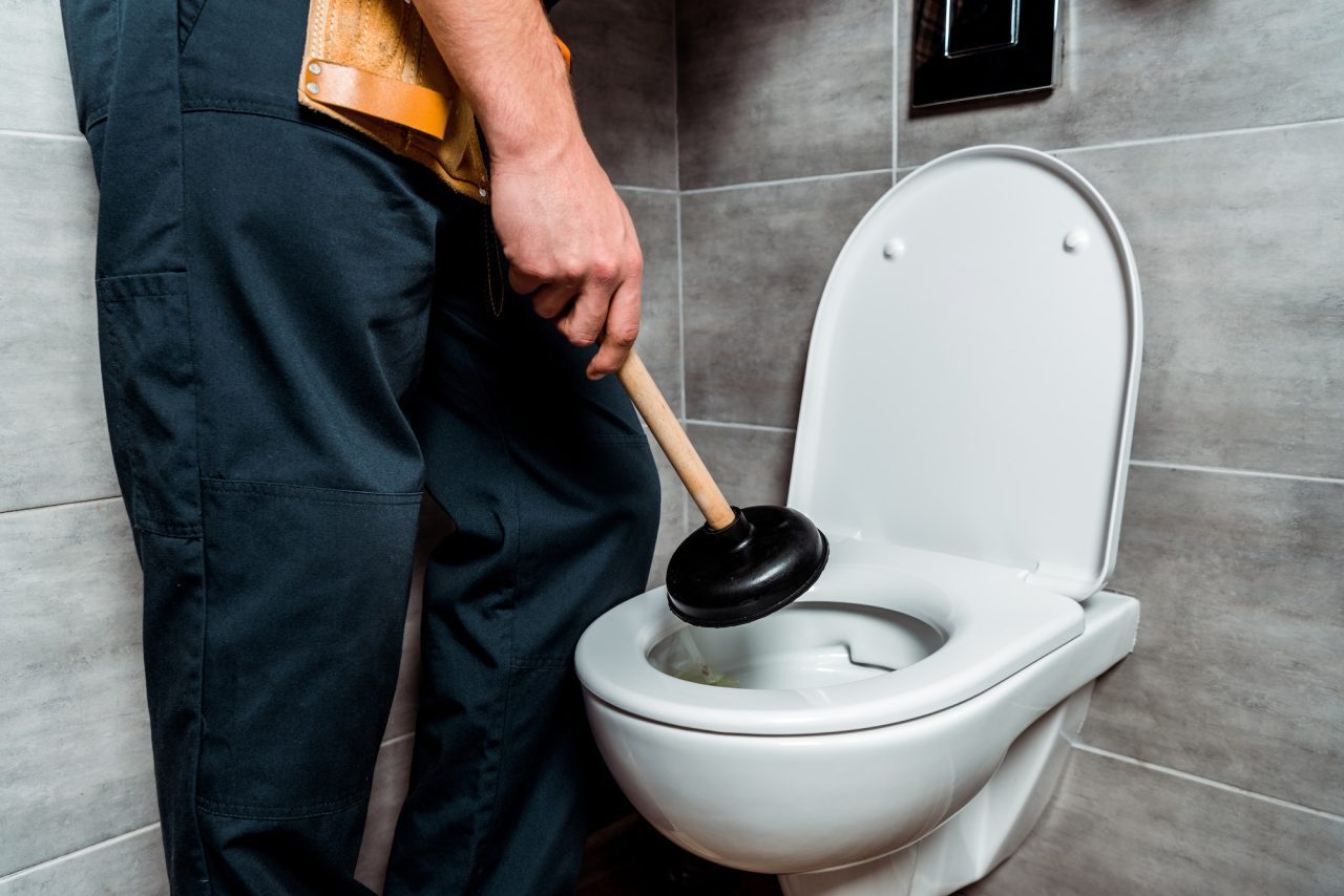 A plumber using a plunger on a clogged toilet, representing prompt repair services available in Lake Forest