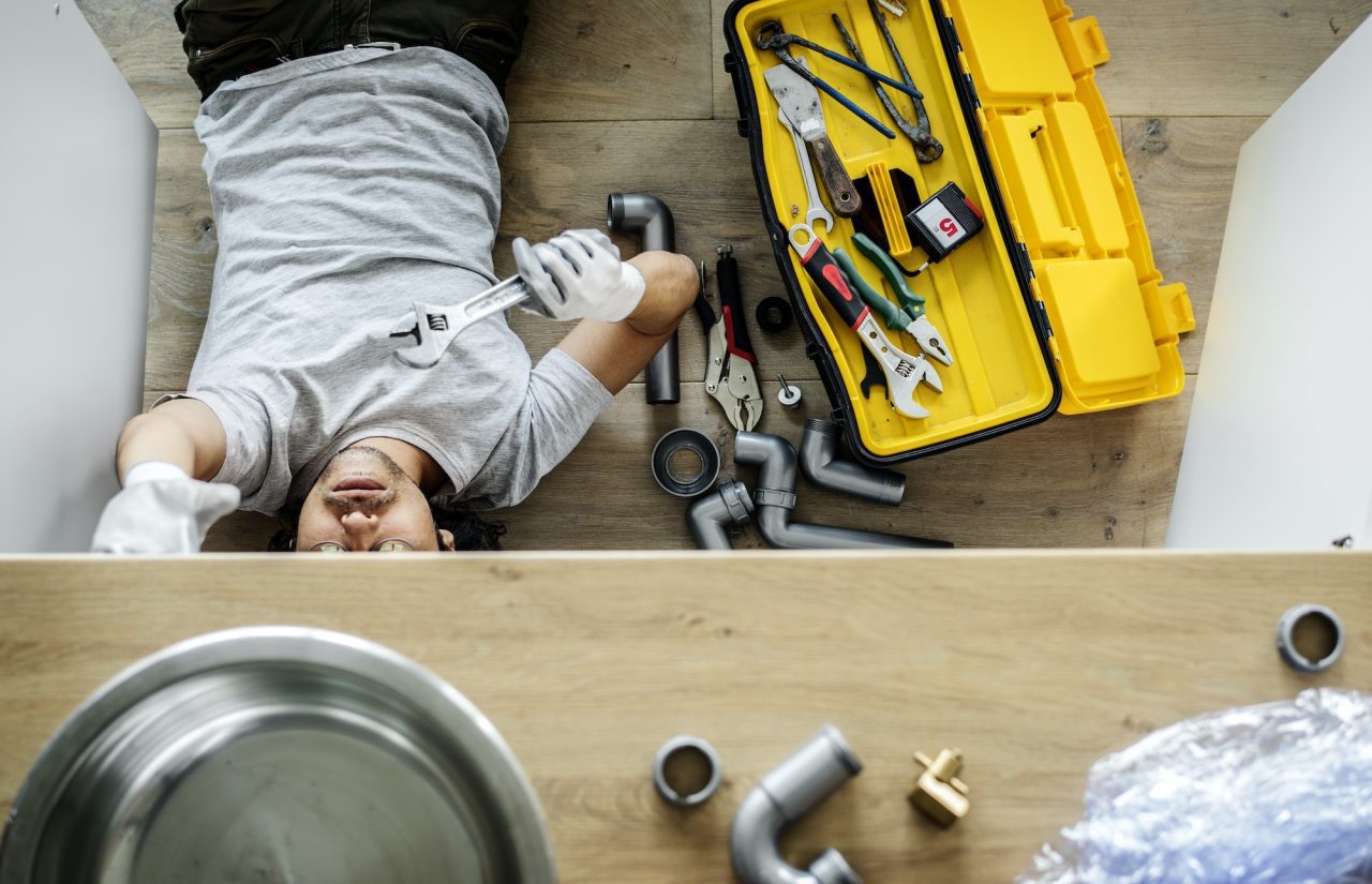 Man fixing leaky kitchen sink drain pipe, a key service offered by Yale the Plumber in Highland Park, IL